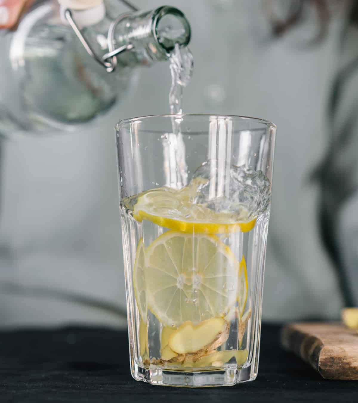 a bottle of water filling a glass of water with slices of lemon