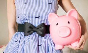 woman's torso wearing a black belt tied in a bow holding a large pink piggy bank