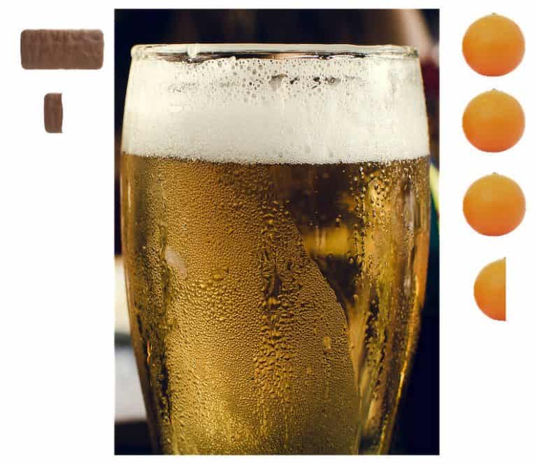 A condensation-covered glass of beer with a frothy head. A chocolate tim tam biscuit plus one-fifth of a tim tam are arranged to the left of the glass and three and one half orange spheres are arranged vertically alongside it, showing the approximate equivalence of calories between the various foods.