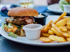 Juicy burger with melted cheese and lettuce on a bun, served with golden fries and dipping sauce on a white plate.