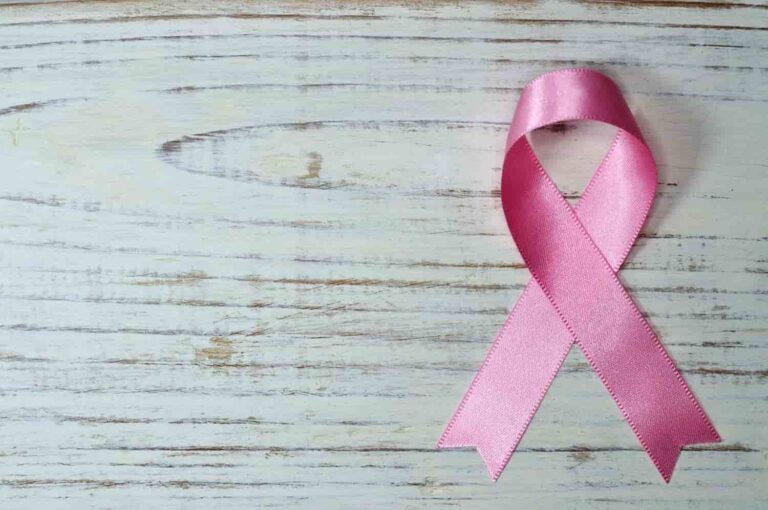 A pink ribbon symbolizing breast cancer awareness is placed on a light wooden surface with visible grains, conveying hope and solidarity.