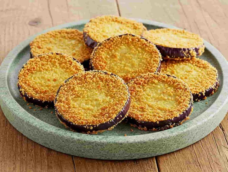 Eggplant slices, coated in golden crispy breadcrumbs, are neatly arranged on a round, light green plate. The background features a rustic wooden table.