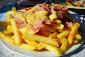 Plate of golden fries topped with melted cheese and diced ham, creating a carbohydrate-heavy dish.