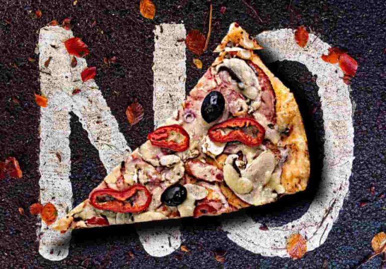 A slice of pizza with mushrooms, olives, and peppers lies on a road with "NO" painted on it, surrounded by scattered autumn leaves.