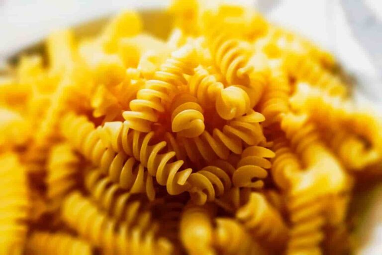 Close-up image of uncooked yellow rotini pasta in soft focus. The spirals are stacked, creating a textured and inviting, warm-toned scene.