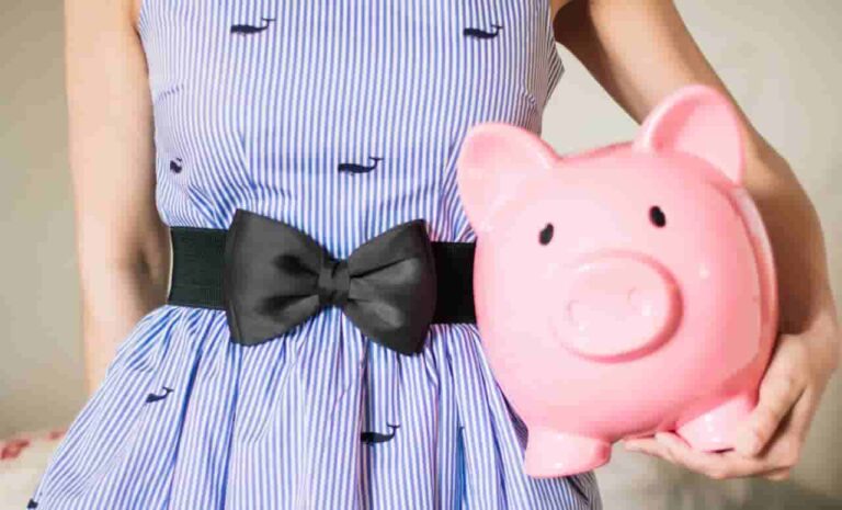 A woman in a blue and white striped dress with small whale patterns and a black bow holds a pink piggy bank, conveying a cheerful and whimsical tone.