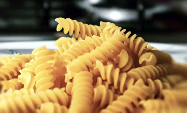 Close-up of a pile of uncooked fusilli pasta on a plate, showcasing its twisted spiral shape.