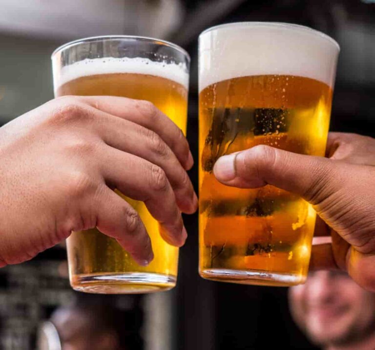 Two male hands clinking glasses filled with frothy amber beer, set against a blurred background.