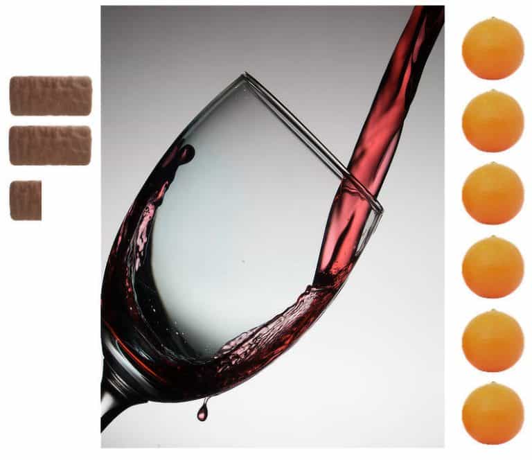 Red wine being poured into a wineglass. To the left of frame, 2.4 tim tams; to the right, six oranges.