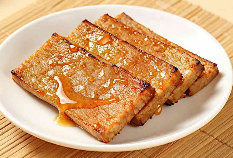 A plate of grilled tempeh slices drizzled with honey rests on a bamboo mat